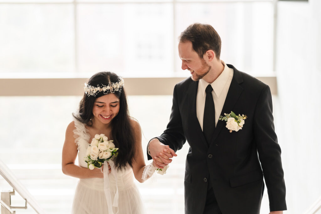 Newlyweds pose by large courthouse windows with natural light, a beautiful interior photography spot at Durham Courthouse for intimate wedding ceremonies.