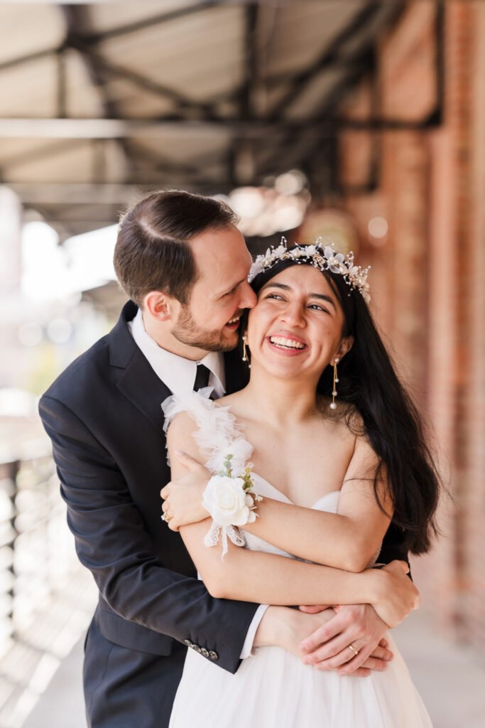 Romantic wedding portrait at the American Tobacco Campus, with the couple framed against a rustic red brick wall, capturing the urban charm of downtown Durham