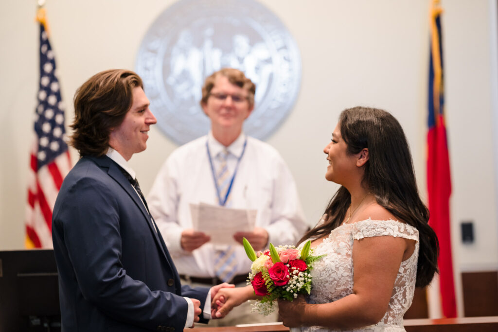 A couple standing in front of the judge, smiling as they exchange vows during their intimate Durham courthouse wedding ceremony.

