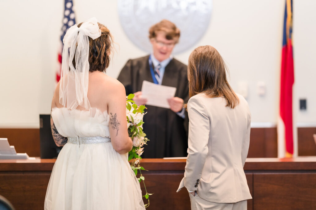 A LGBTQ+ couple standing in front of the judge, looking at the judge as he was going through the paperwork in intimate Durham courthouse wedding ceremony.

